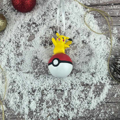 A personalized Pokémon Pikachu ornament standing on a red and white Poké Ball, with a name and year hand-written on the base.