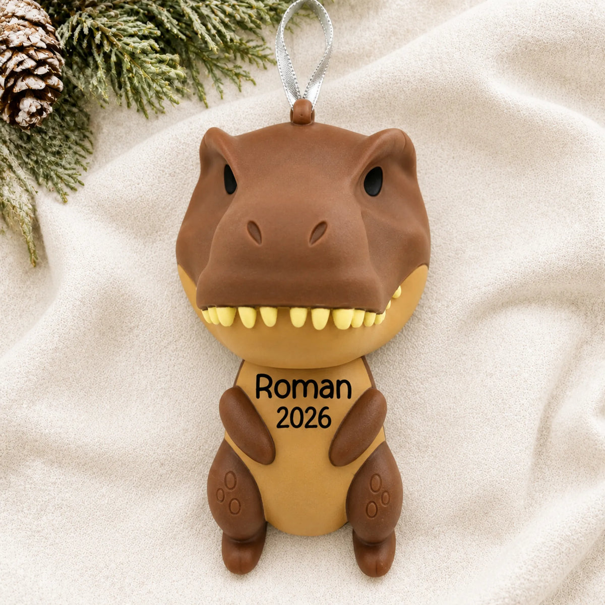 Personalized brown t-rex dinosaur christmas ornament laid on a soft white knit blanket