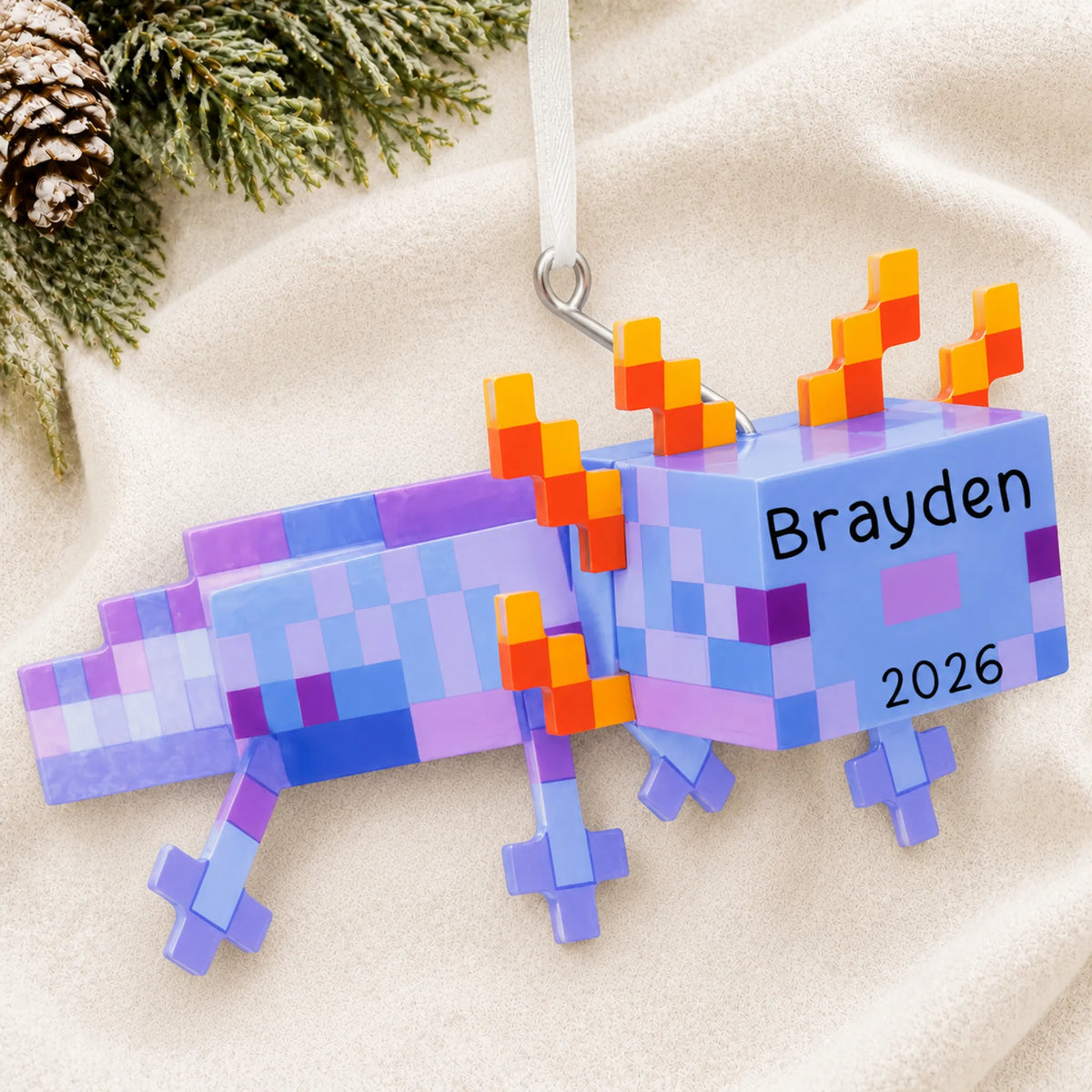 Personalized pixel video game axolotl christmas ornament laid on a soft white knit blanket
