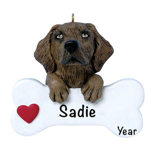 Personalized Chocolate Lab Christmas ornament, the dog resting its head and paws on a white dog bone with a red heart, the pet name laser engraved across the bone and the year below it