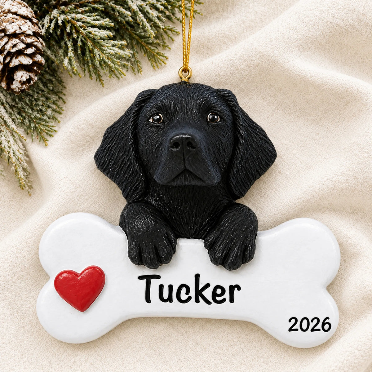 Personalized black Lab dog bone Christmas ornament resting on a soft white blanket with pine and pinecones
