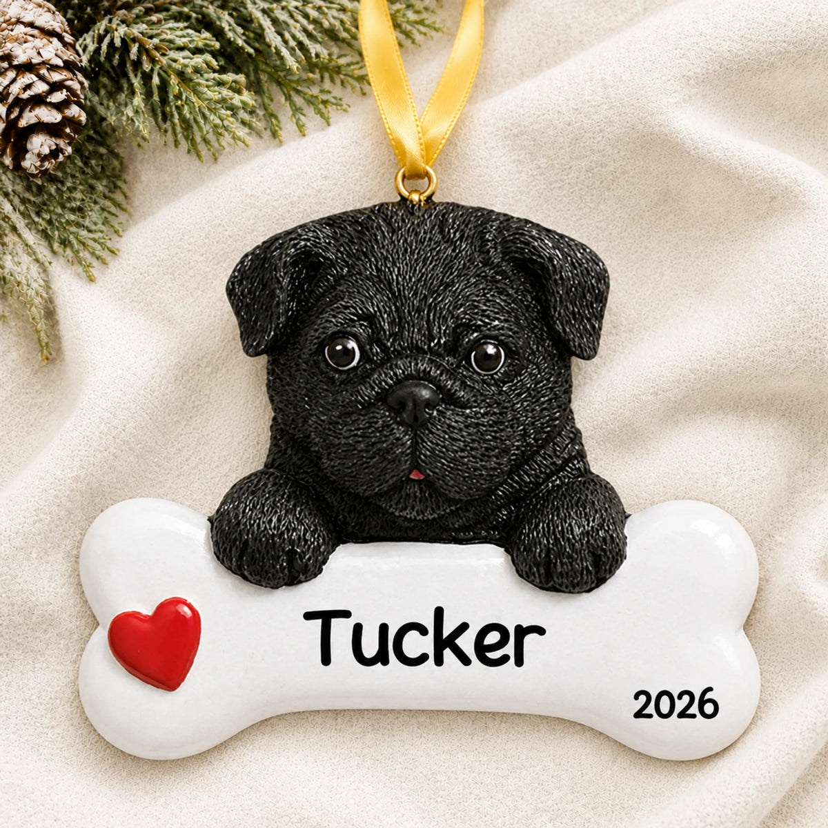 Personalized black pug dog bone Christmas ornament resting on a soft white blanket with pine and pinecones