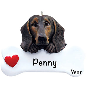 Personalized Black & Tan Dachshund Christmas ornament, the dog resting its head and paws on a white dog bone with a red heart, the pet name laser engraved across the bone and the year below it