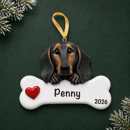 Personalized black and tan dachshund dog bone Christmas ornament, engraved with a name and year, on a green holiday backdrop