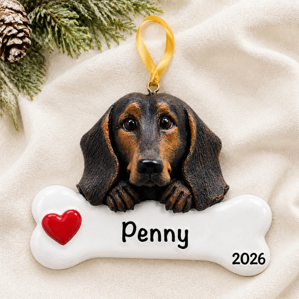 Personalized black and tan dachshund dog bone Christmas ornament resting on a soft white blanket with pine and pinecones