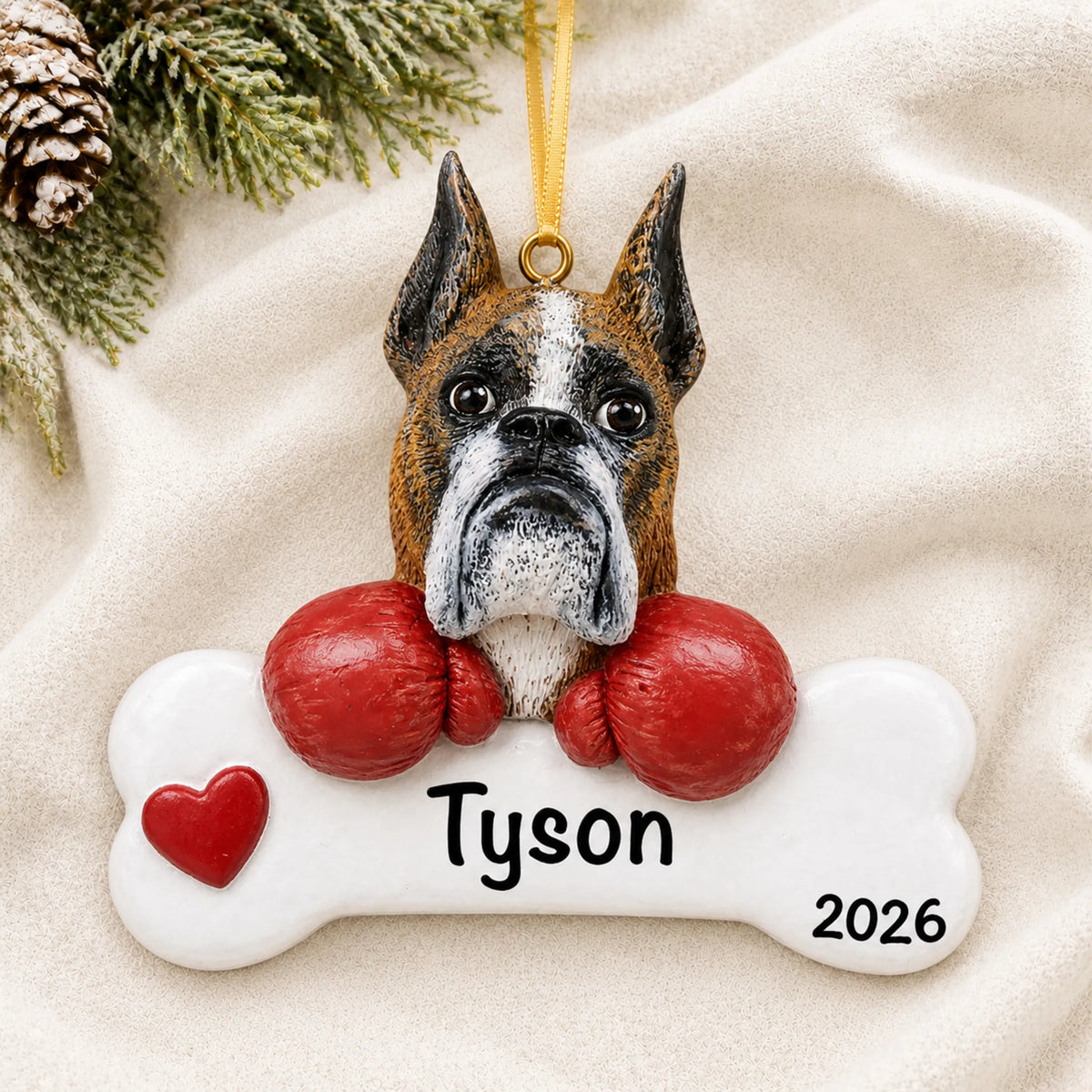 Personalized boxer dog bone Christmas ornament resting on a soft white blanket with pine and pinecones