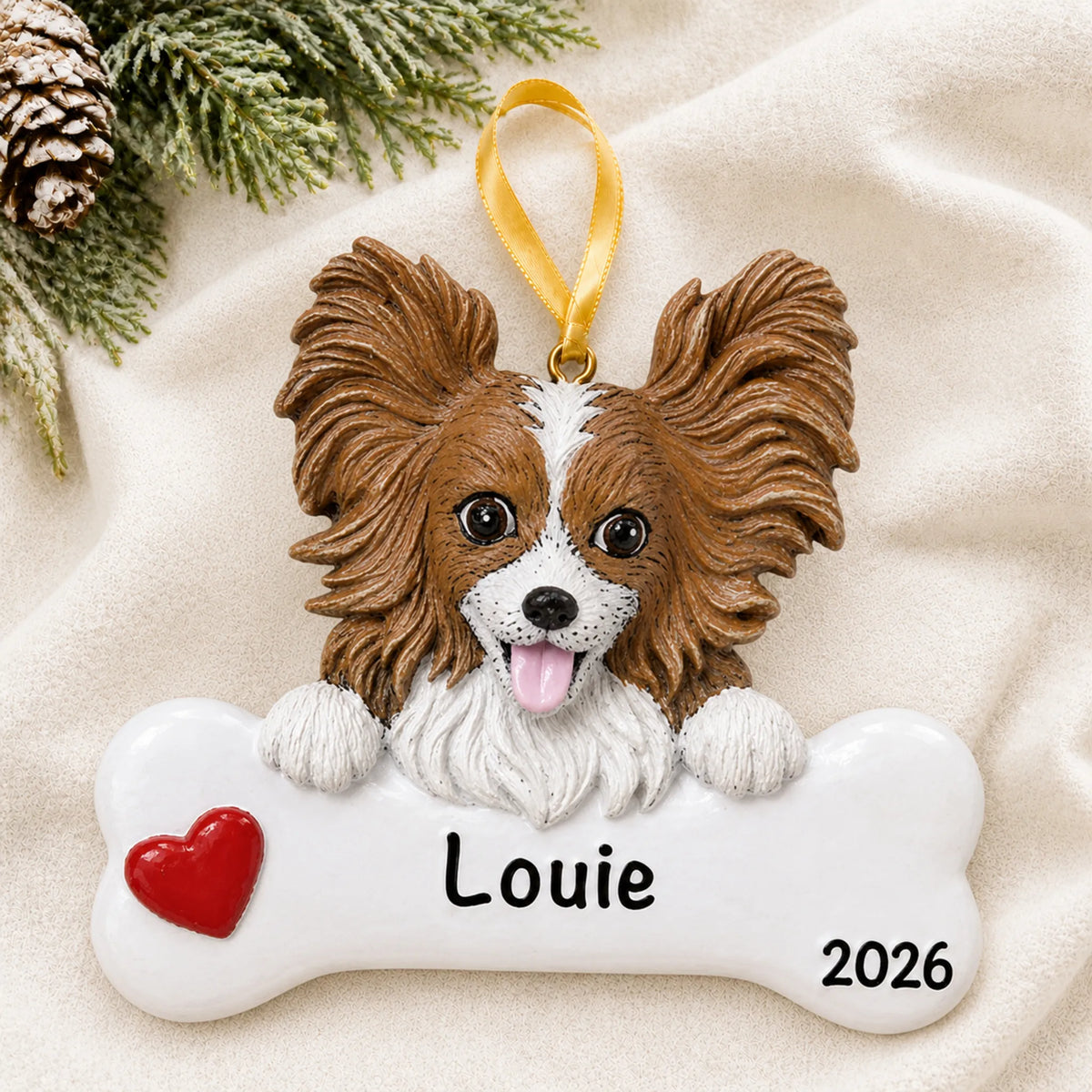 Personalized papillon dog bone Christmas ornament resting on a soft white blanket with pine and pinecones