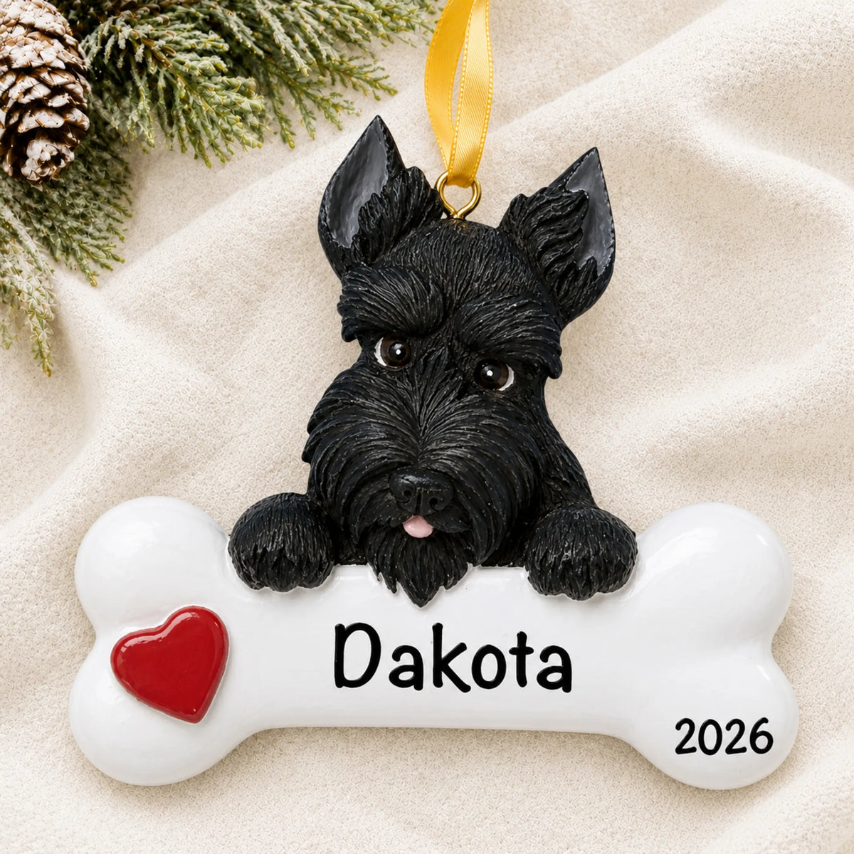 Personalized Scottie dog bone Christmas ornament resting on a soft white blanket with pine and pinecones