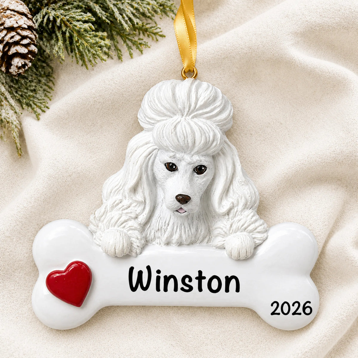 Personalized white poodle dog bone Christmas ornament resting on a soft white blanket with pine and pinecones