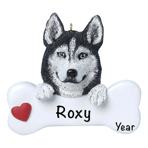Personalized Siberian Husky Christmas ornament, the dog resting its head and paws on a white dog bone with a red heart, the pet name laser engraved across the bone and the year below it