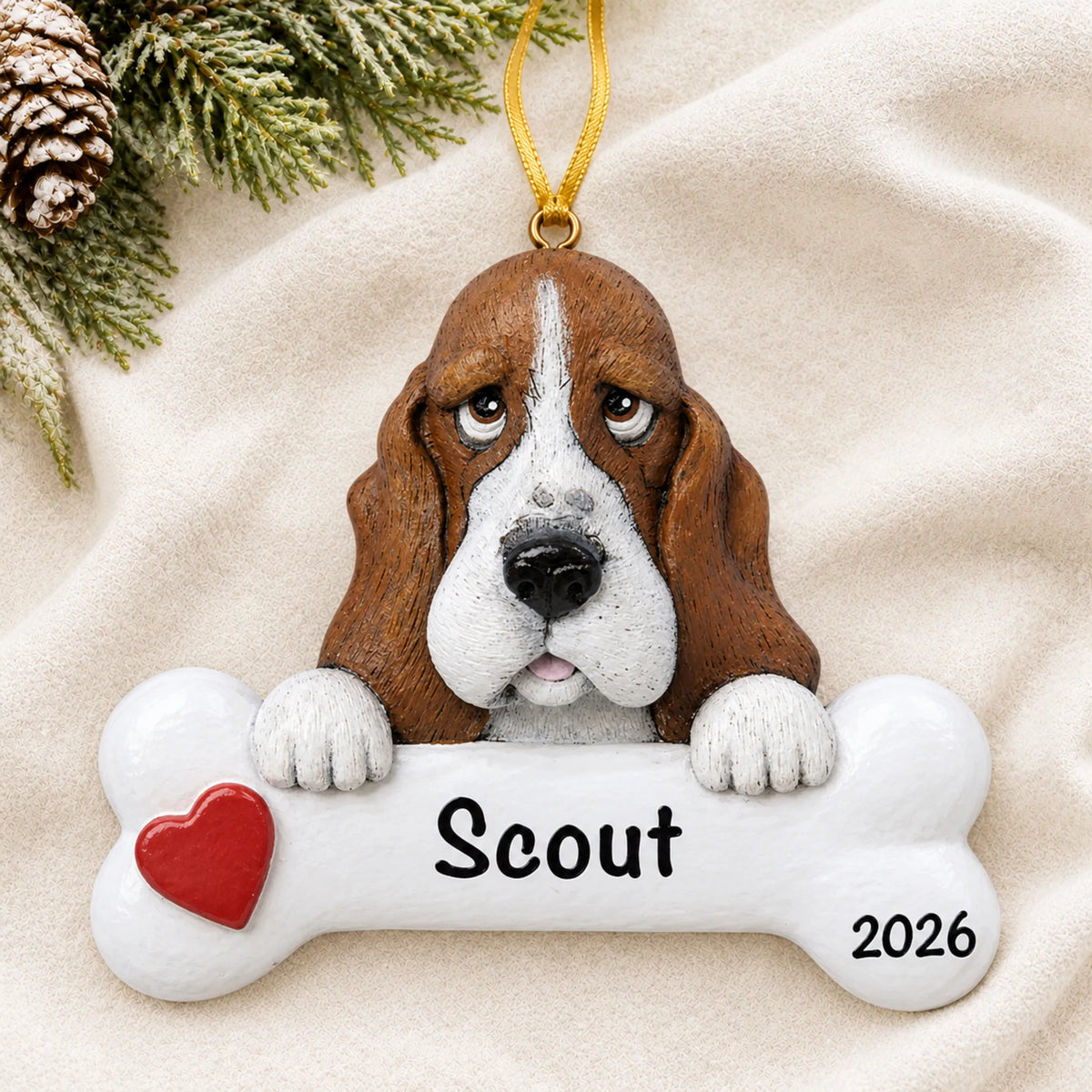 Personalized basset hound dog bone Christmas ornament resting on a soft white blanket with pine and pinecones