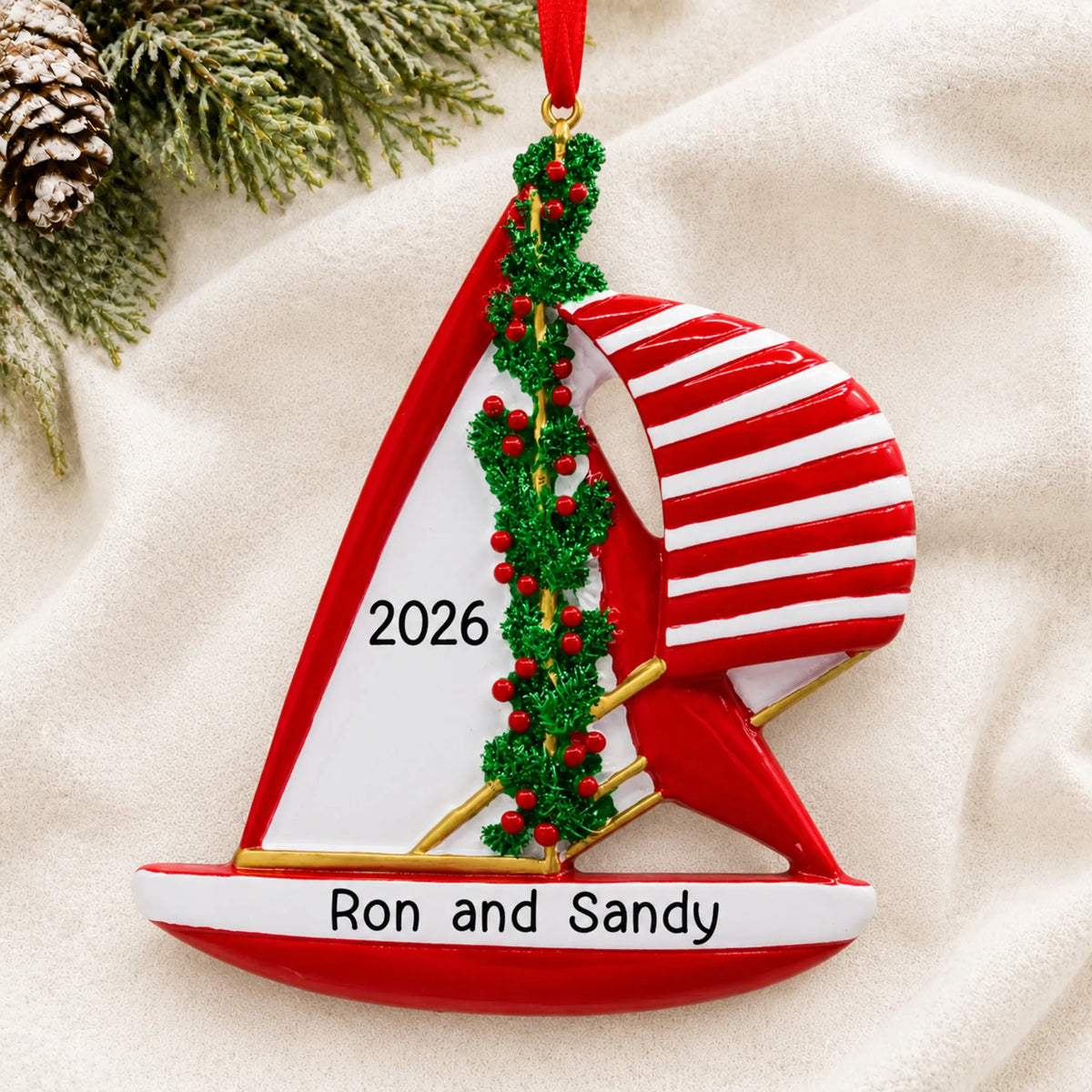 Personalized red sailboat christmas ornament laid on a soft white knit blanket