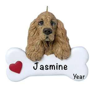 Personalized Cocker Spaniel Christmas ornament, the dog resting its head and paws on a white dog bone with a red heart, the pet name laser engraved across the bone and the year below it