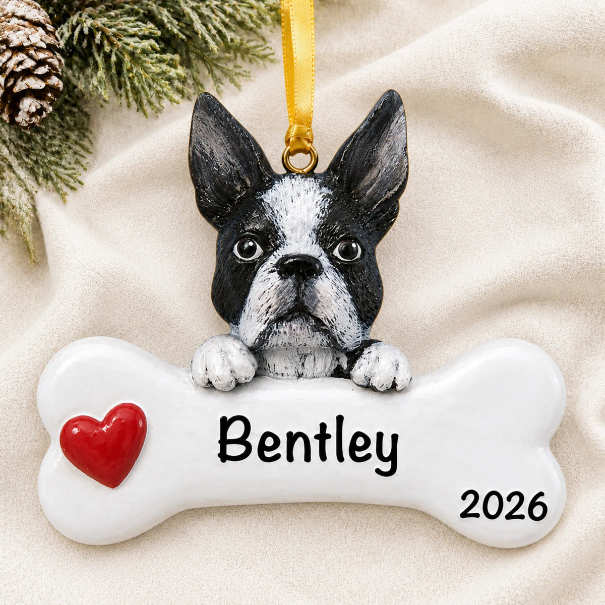 Personalized Boston terrier dog bone Christmas ornament resting on a soft white blanket with pine and pinecones