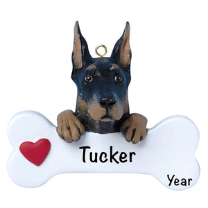 Personalized Doberman Pinscher Christmas ornament, the dog resting its head and paws on a white dog bone with a red heart, the pet name laser engraved across the bone and the year below it