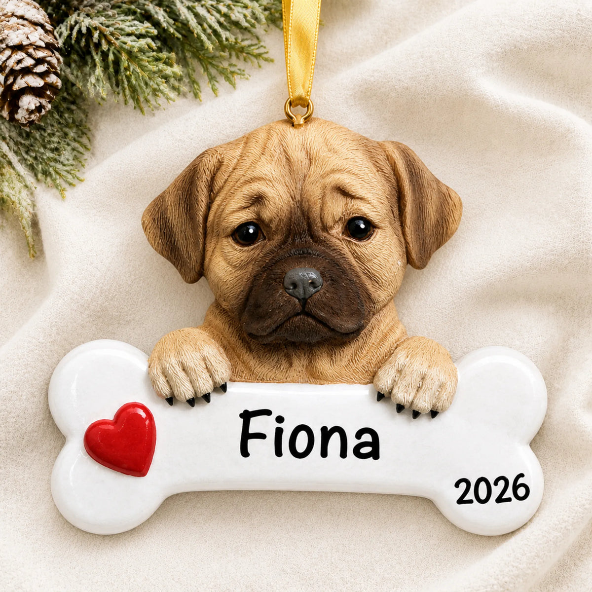 Personalized puggle dog bone Christmas ornament resting on a soft white blanket with pine and pinecones