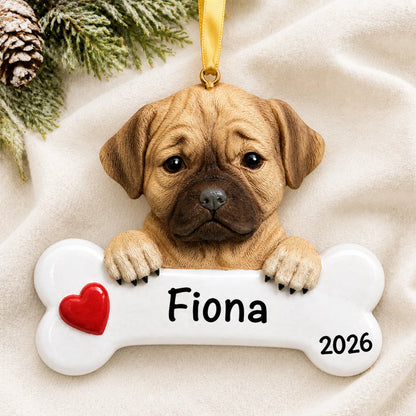 Personalized puggle dog bone Christmas ornament resting on a soft white blanket with pine and pinecones
