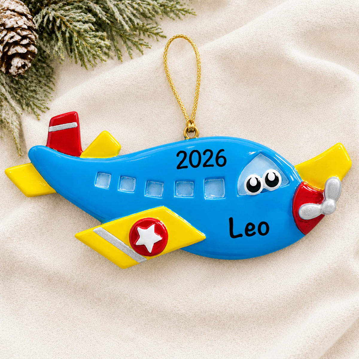 Personalized blue airplane christmas ornament laid on a soft white knit blanket