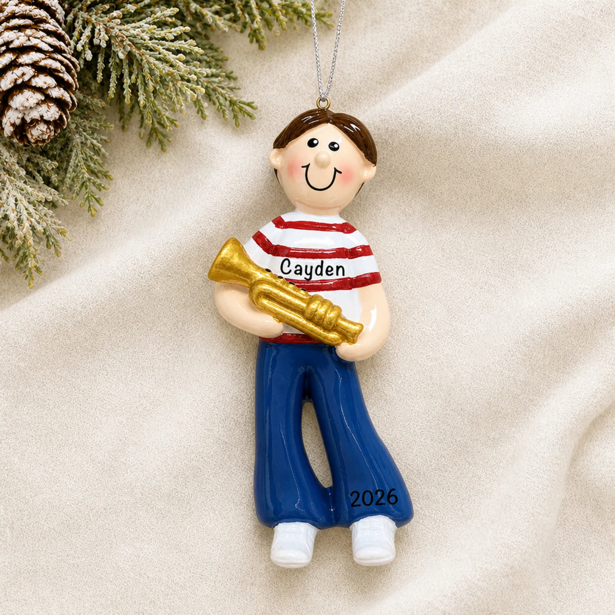 Personalized trumpet boy christmas ornament laid on a soft white knit blanket
