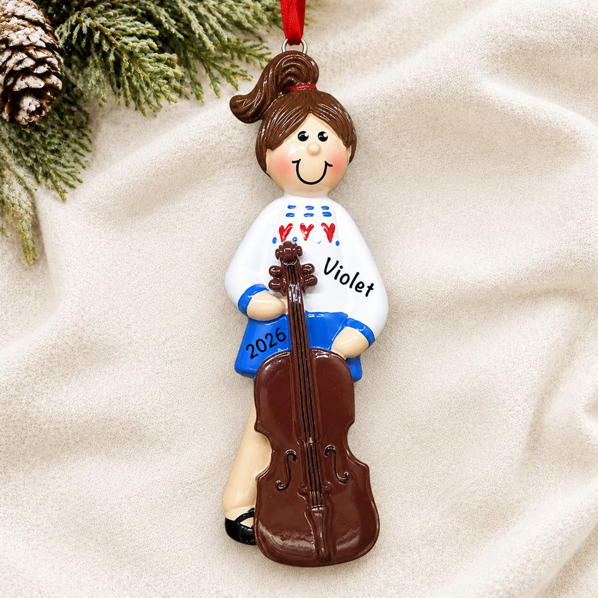 Personalized cello girl christmas ornament laid on a soft white knit blanket