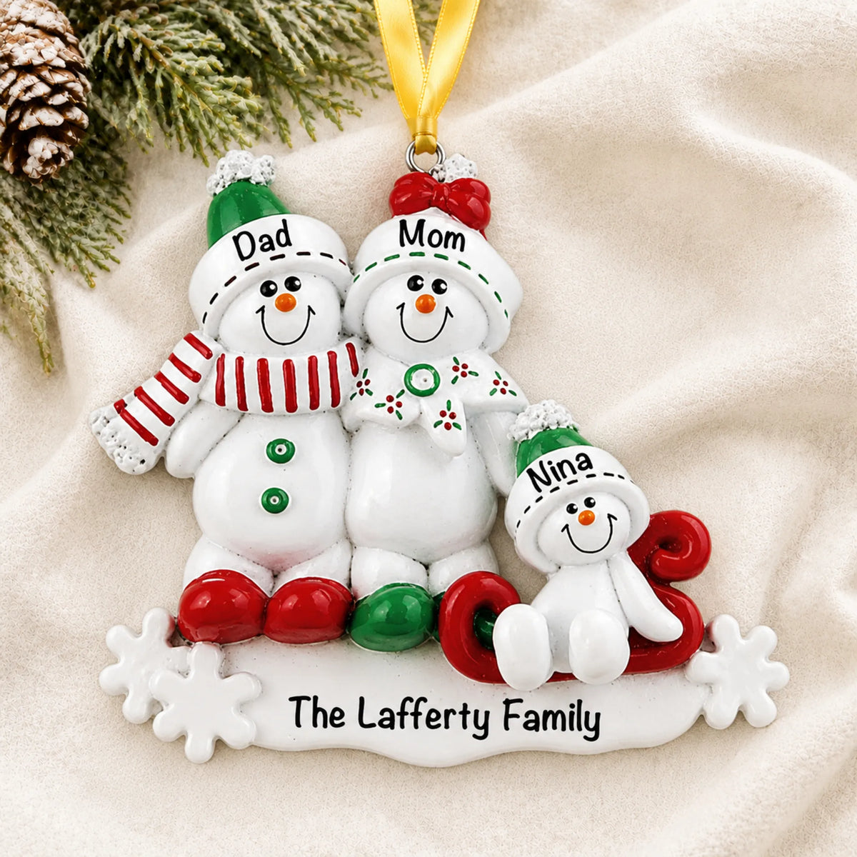 Personalized snowman sled family of 3 christmas ornament laid on a soft white knit blanket
