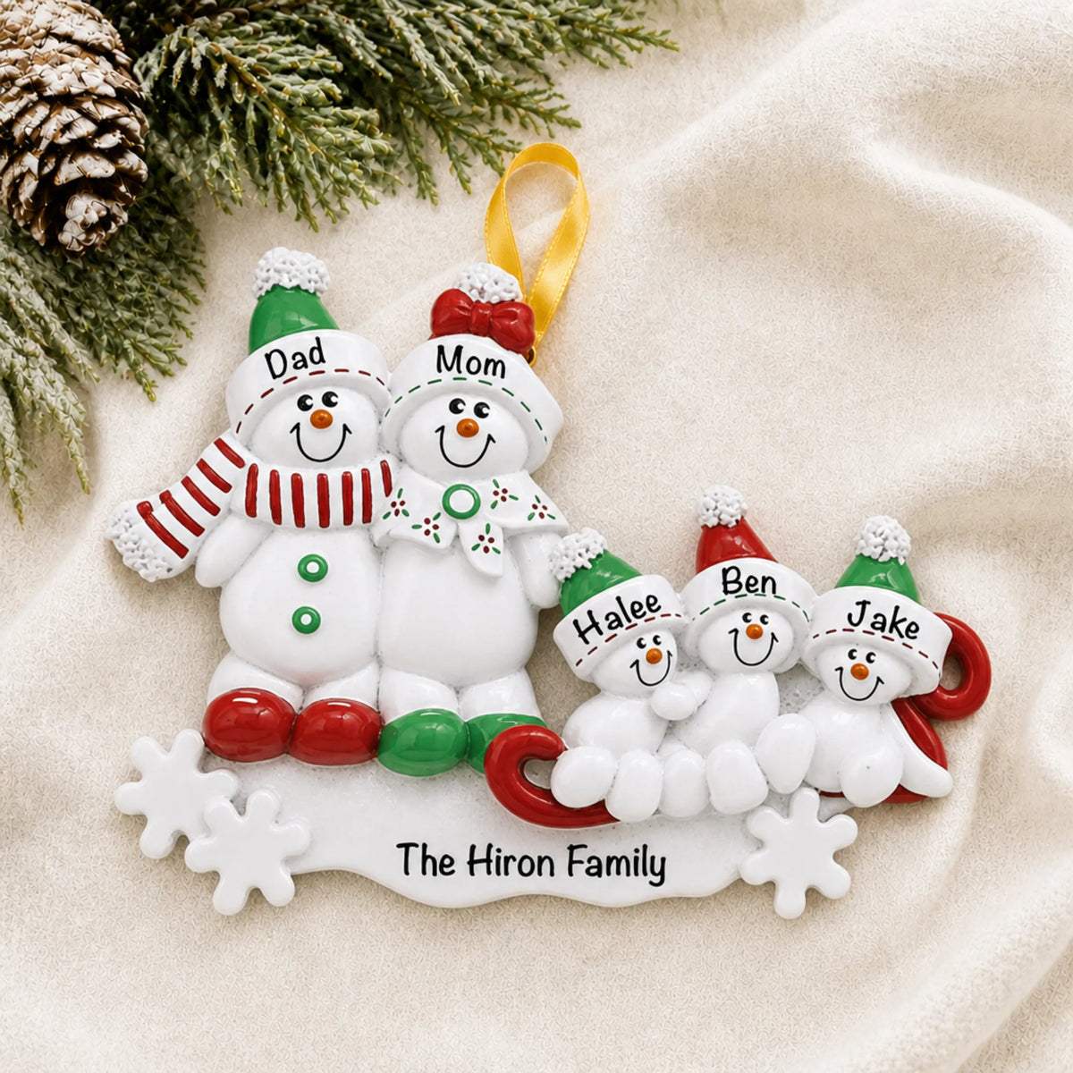 Personalized snowman sled family of 5 christmas ornament laid on a soft white knit blanket