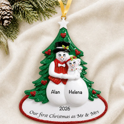 Personalized newlywed snow couple Christmas ornament on a cream knit blanket beside pine and pinecones