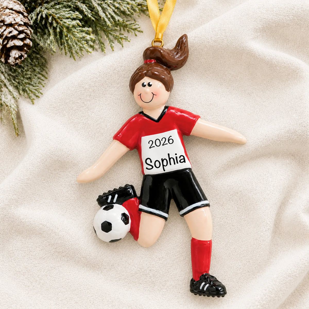 Personalized brunette soccer girl christmas ornament laid on a soft white knit blanket