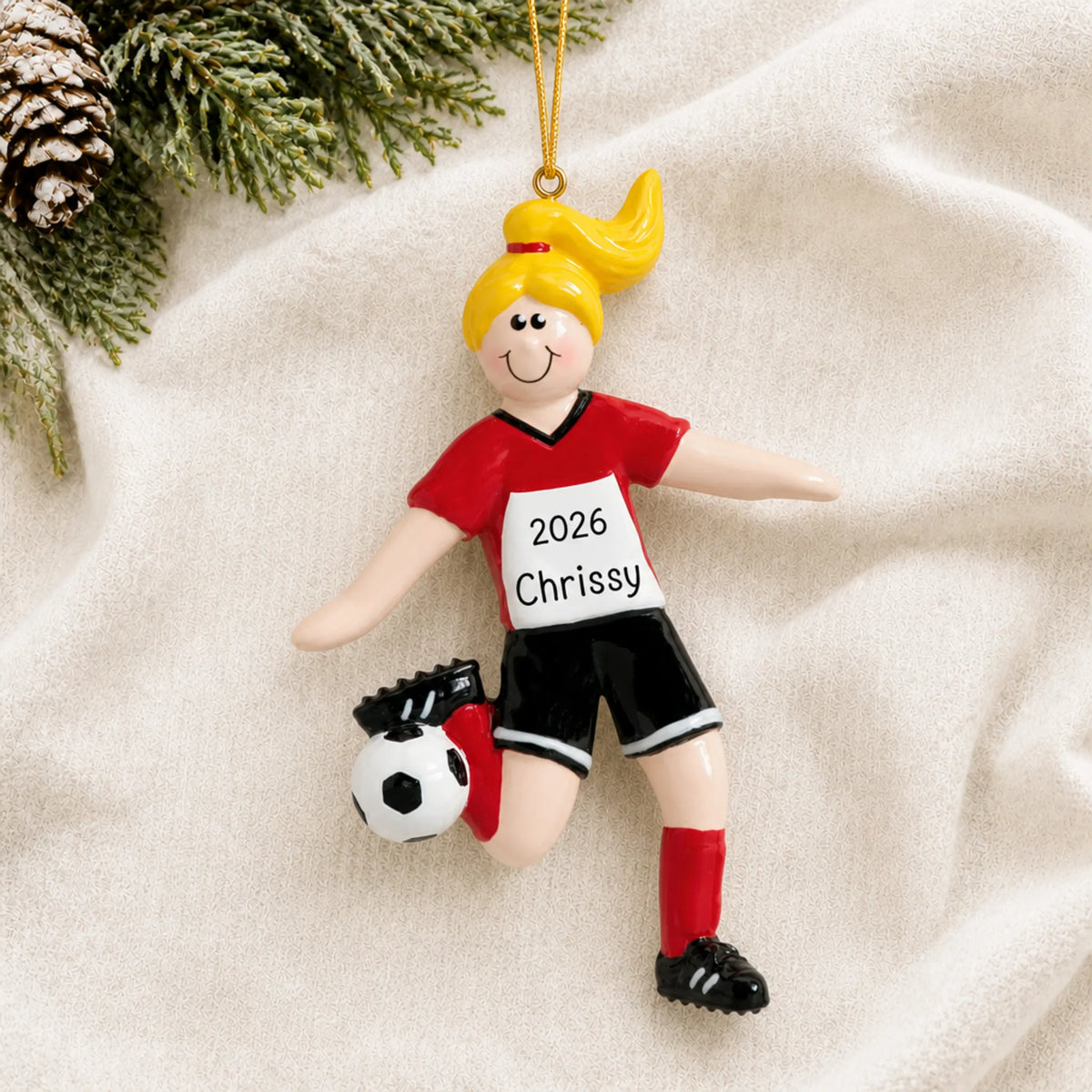 Personalized blonde soccer girl christmas ornament laid on a soft white knit blanket