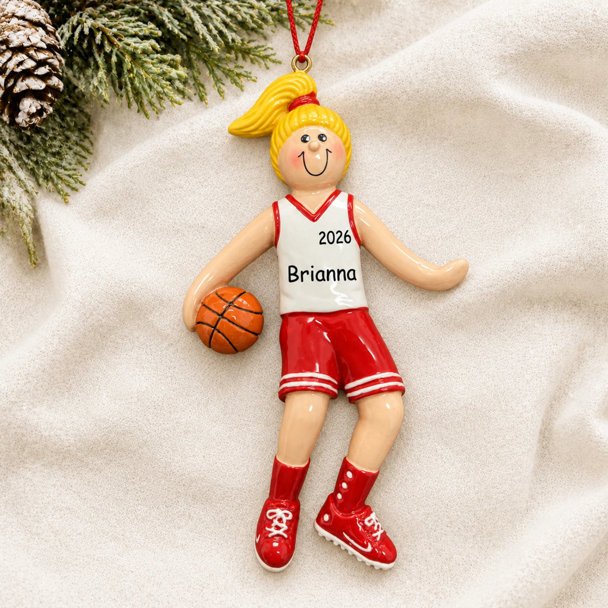 Personalized blonde basketball girl christmas ornament laid on a soft white knit blanket
