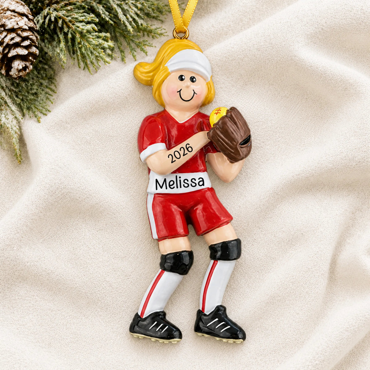 Personalized blonde softball girl christmas ornament laid on a soft white knit blanket