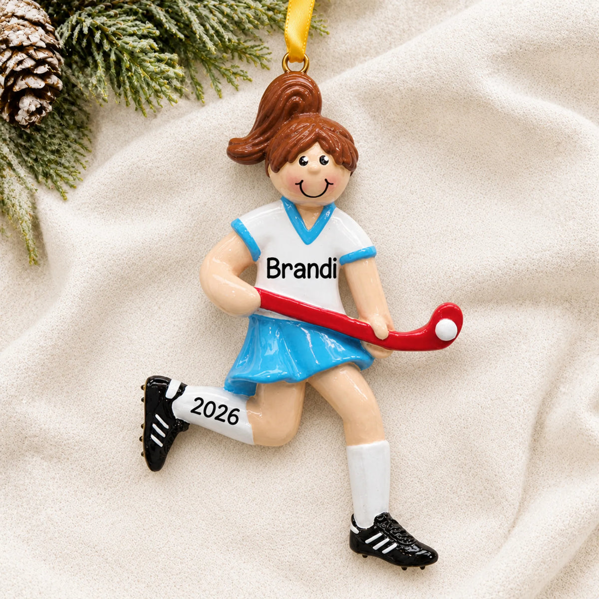 Personalized field hockey girl christmas ornament laid on a soft white knit blanket