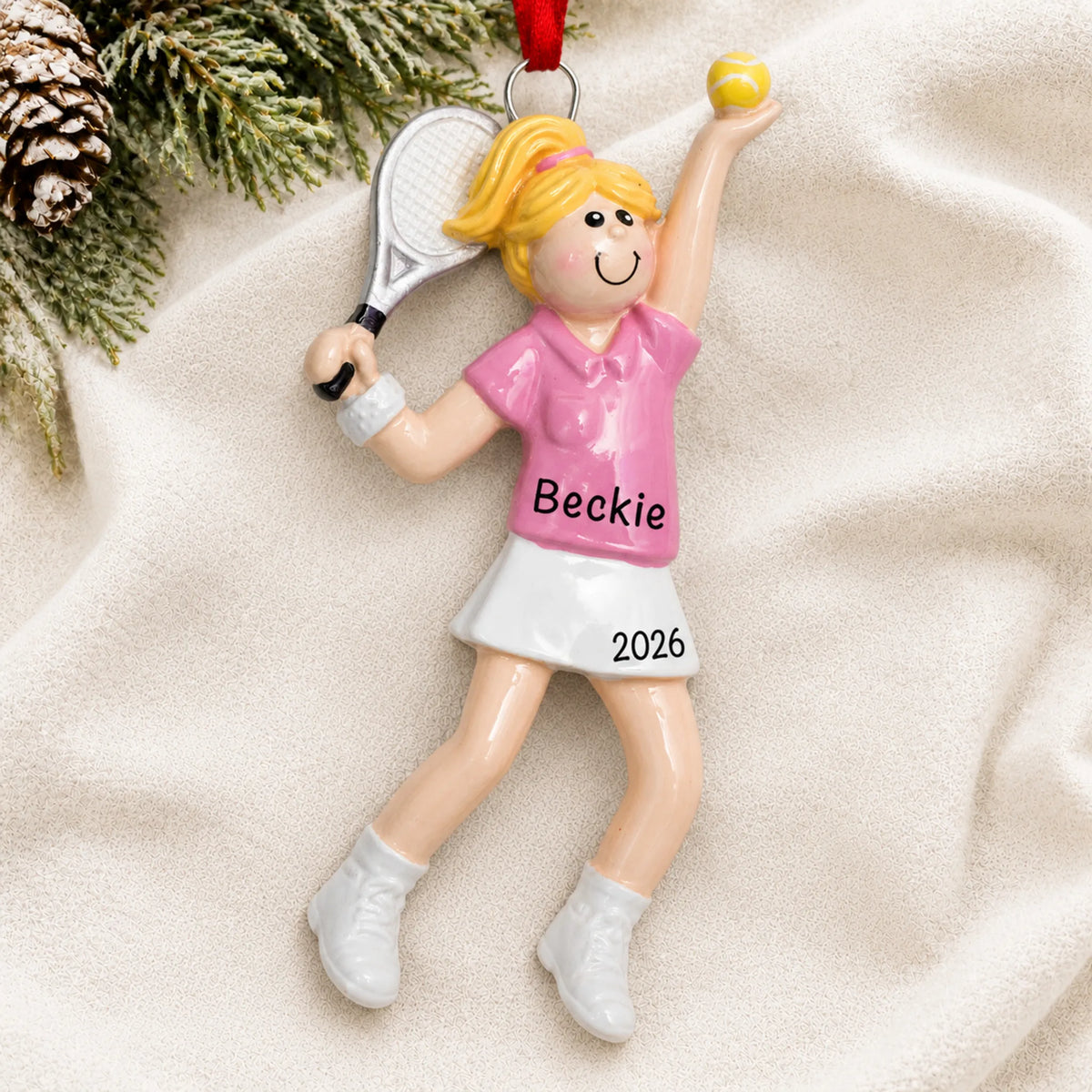 Personalized blonde tennis girl christmas ornament laid on a soft white knit blanket