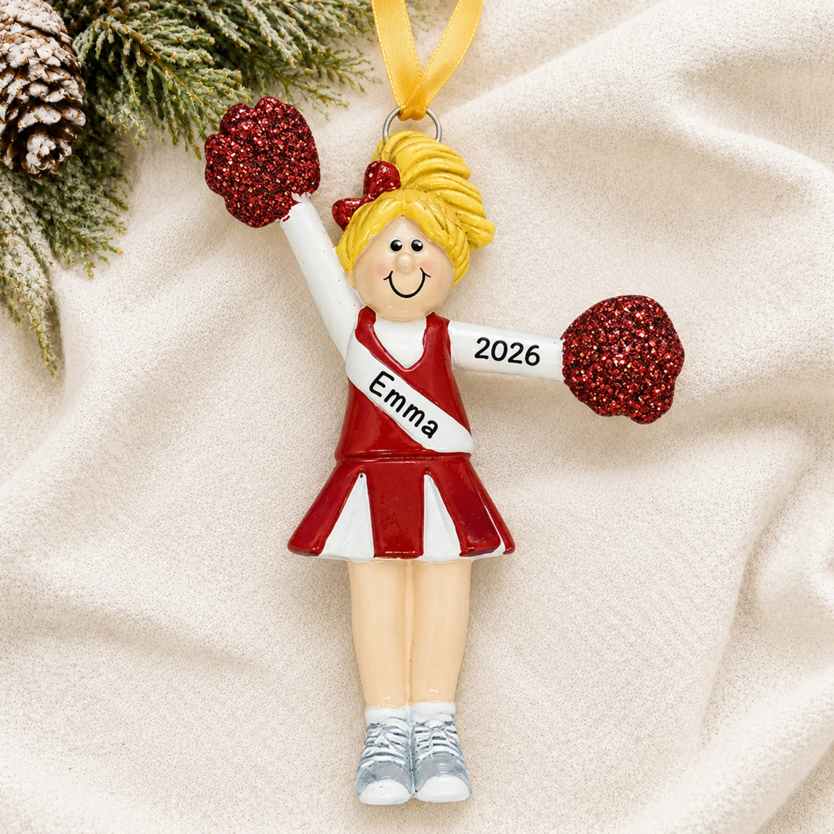 Personalized blonde pom pom cheerleader christmas ornament laid on a soft white knit blanket