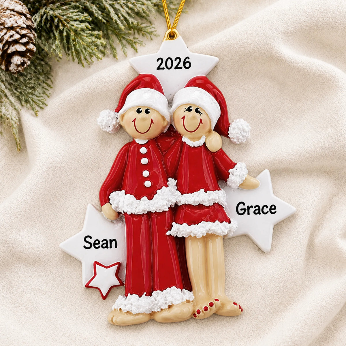 Personalized christmas pajama couple ornament laid on a soft white knit blanket