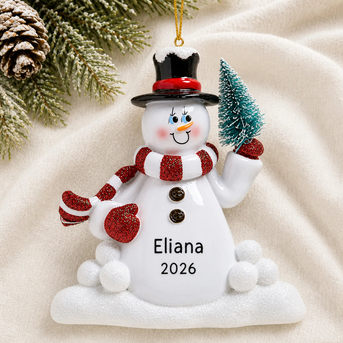 Personalized Snowman with Tree christmas ornament laid on a soft white knit blanket