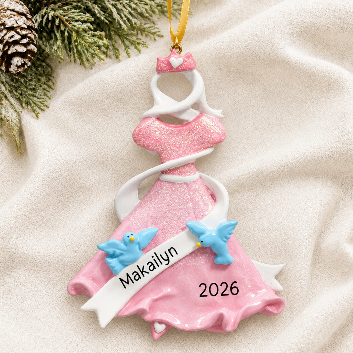 Personalized pink princess dress christmas ornament laid on a soft white knit blanket