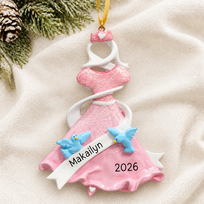 Personalized pink princess dress christmas ornament laid on a soft white knit blanket