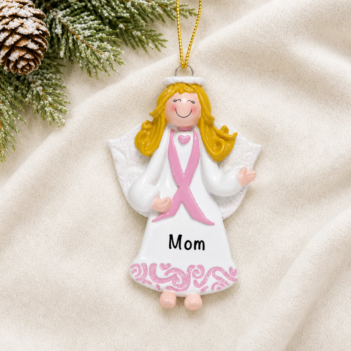 Personalized Pink Ribbon Angel christmas ornament laid on a soft white knit blanket