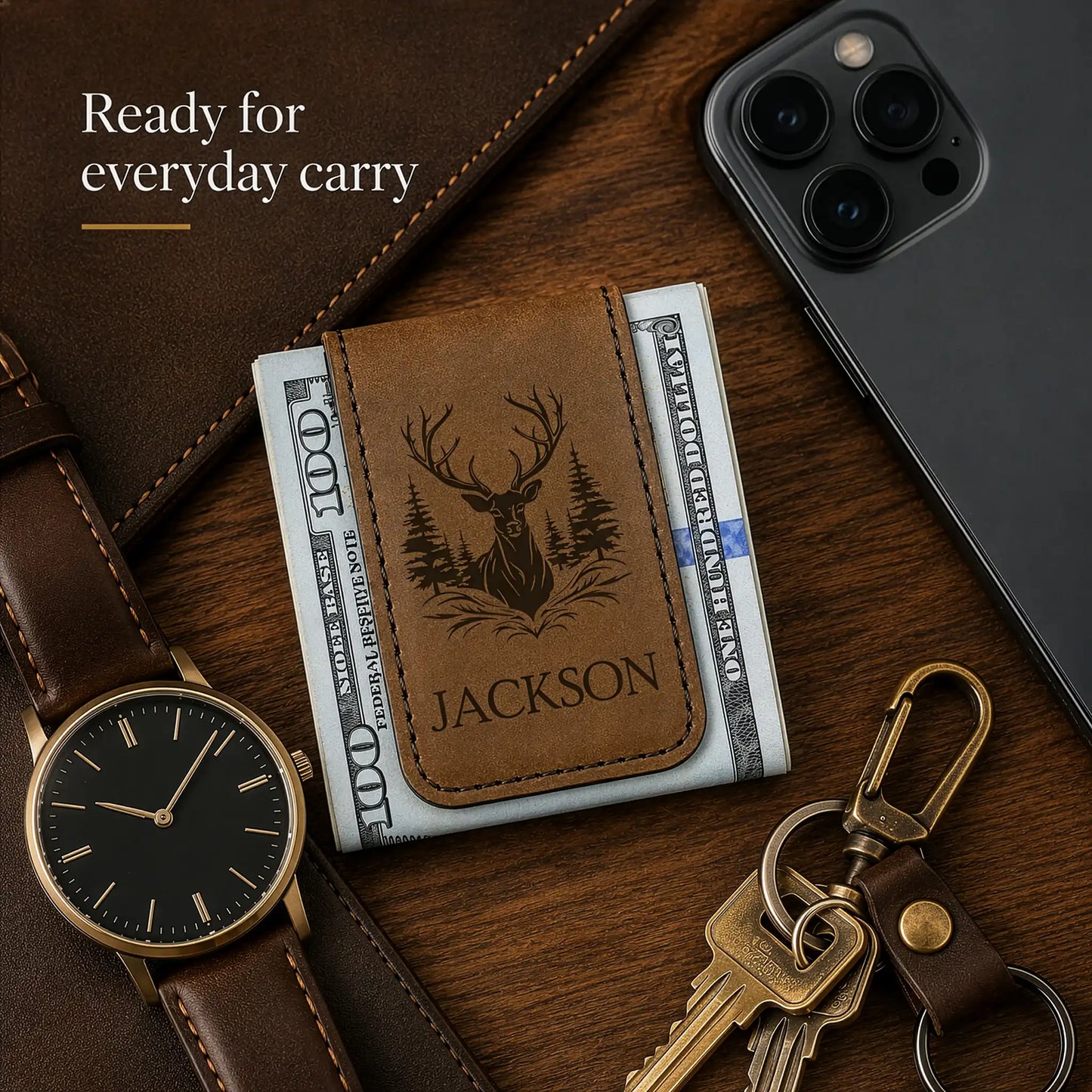 Brown leather wallet with deer design and 'Jackson' engraving, surrounded by phone, keys, and watch on wooden surface.