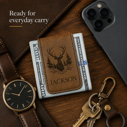 Brown leather wallet with deer design and 'Jackson' engraving, surrounded by phone, keys, and watch on wooden surface.