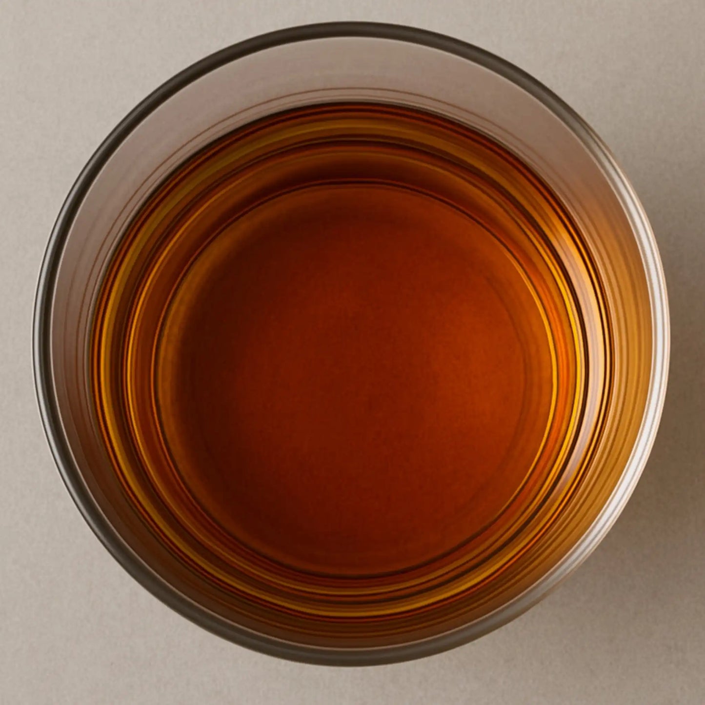 Top-down view of personalized whiskey rocks glass filled with amber whiskey on a neutral background
