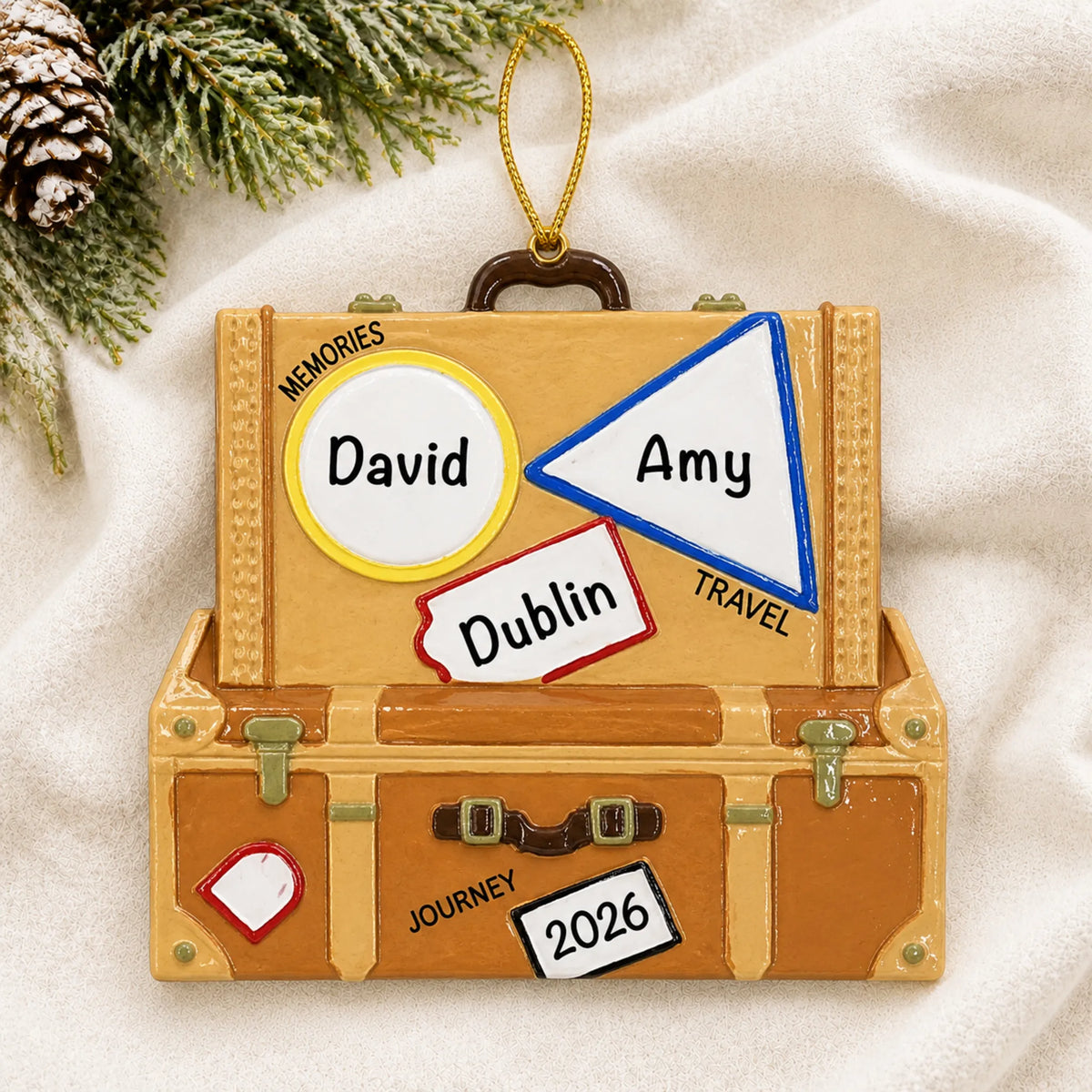 Personalized travel suitcase christmas ornament laid on a soft white knit blanket