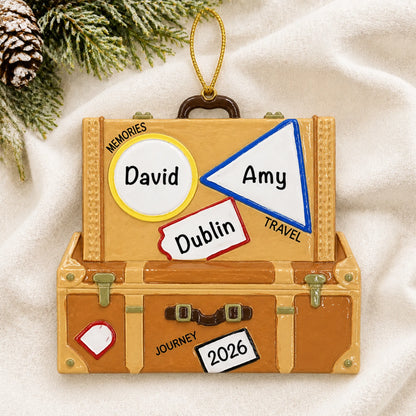 Personalized travel suitcase christmas ornament laid on a soft white knit blanket