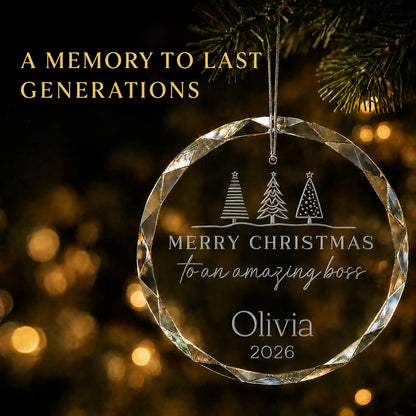 Personalized Amazing Boss glass Christmas ornament hanging on a lit tree, engraved with Christmas trees, the boss's name and year