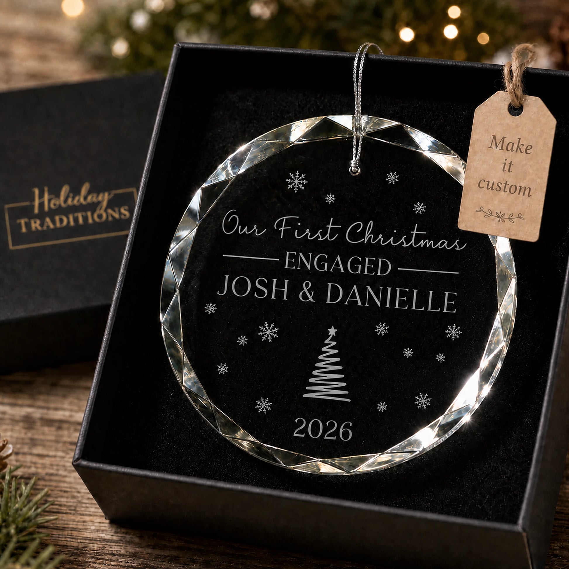 Our First Christmas Engaged personalized glass ornament with a Christmas tree and snowflakes, laser engraved with the couple's names and year, shown in its black gift box