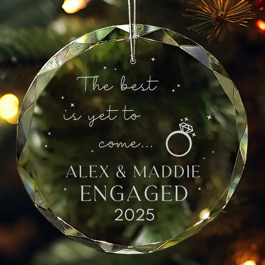 Personalized glass ornament engraved with “The best is yet to come with Names and Year of engagement” hanging on Christmas tree