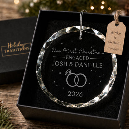 Our First Christmas Engaged personalized glass ornament with two rings, laser engraved with the couple's names and year, shown in its black gift box