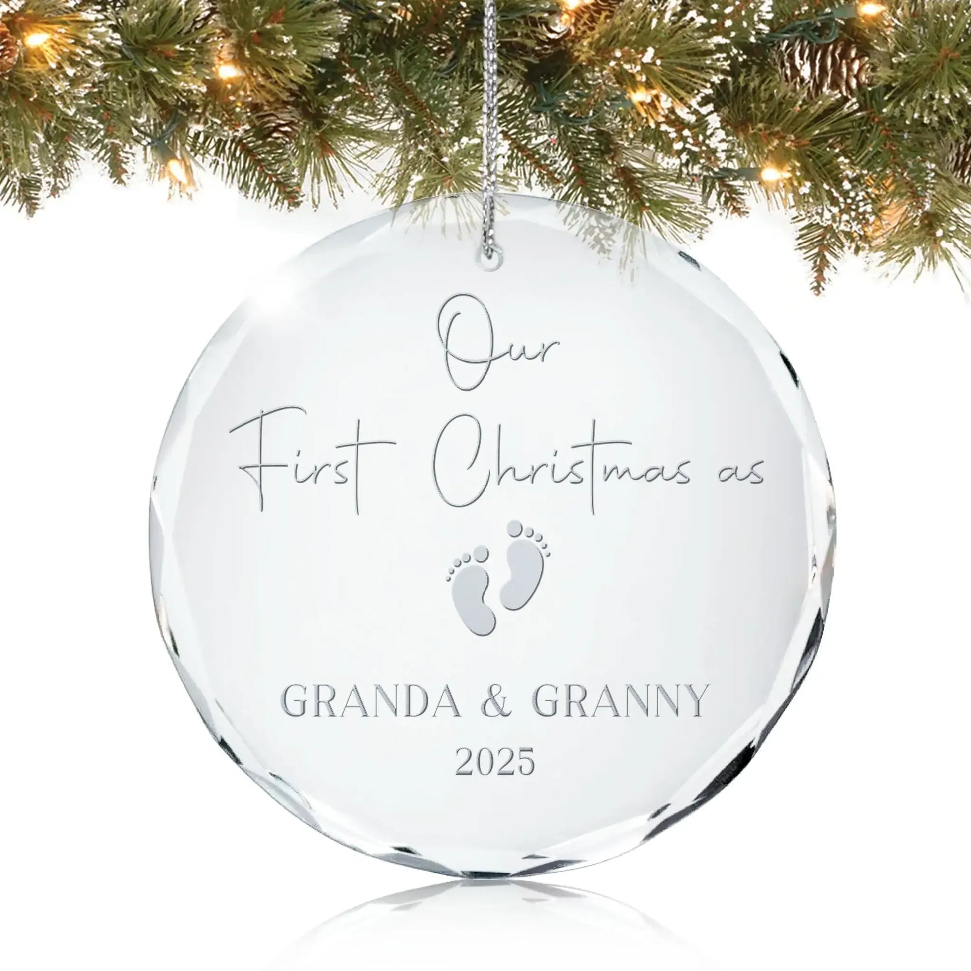 Personalized glass ornament engraved with “Our First Christmas as Granda & Granny 2025” and baby footprints design, hanging on a Christmas tree.