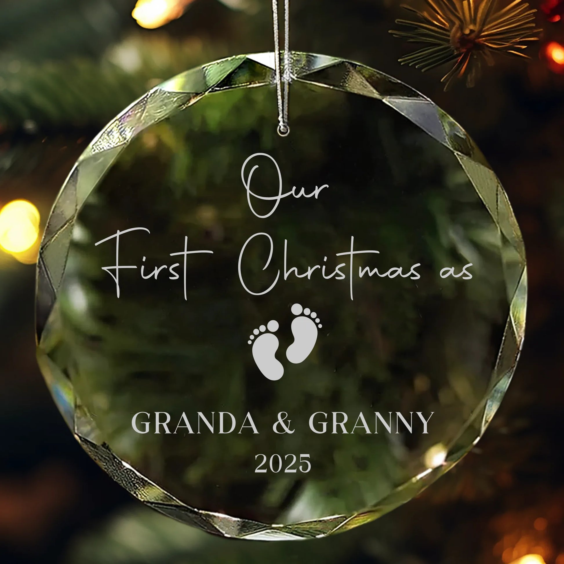 Personalized glass ornament engraved with “Our First Christmas as Granda & Granny 2025” and baby footprints design, hanging on a Christmas tree.